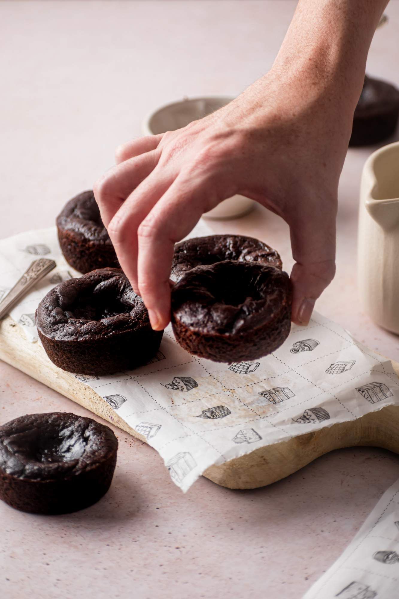 Paleo chocolate pumpkin brownies being picked up by a hand off a wooden cutting board.