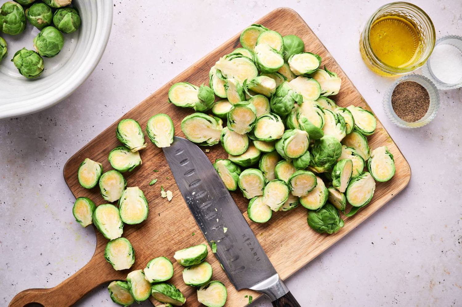 Cutting board with sliced brussels sprouts, olive oil, salt, and pepper.