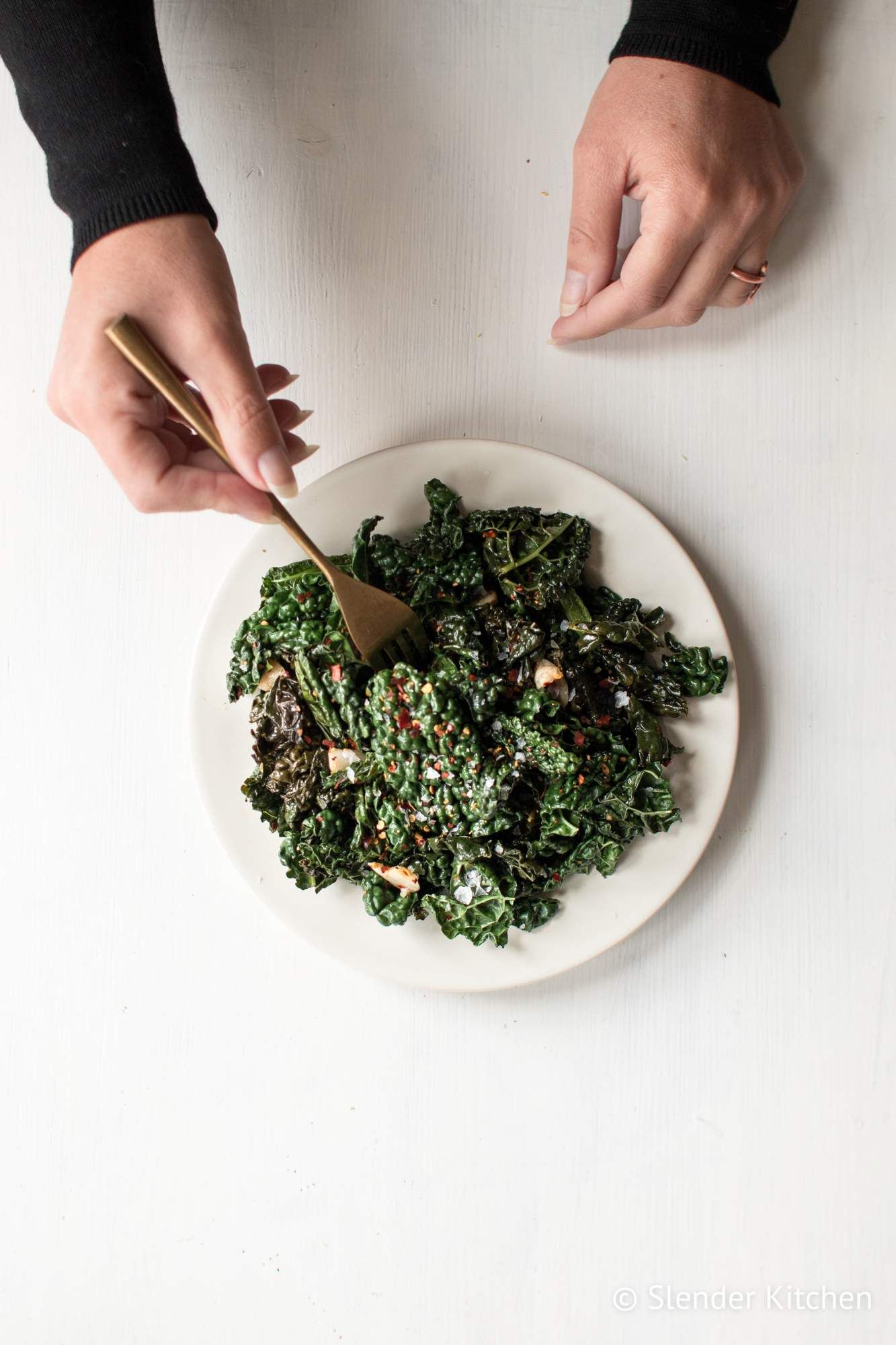 Kale that has been sauteed with olive oil, garlic, red pepper flakes, and vinegar in a dish being held by hands.