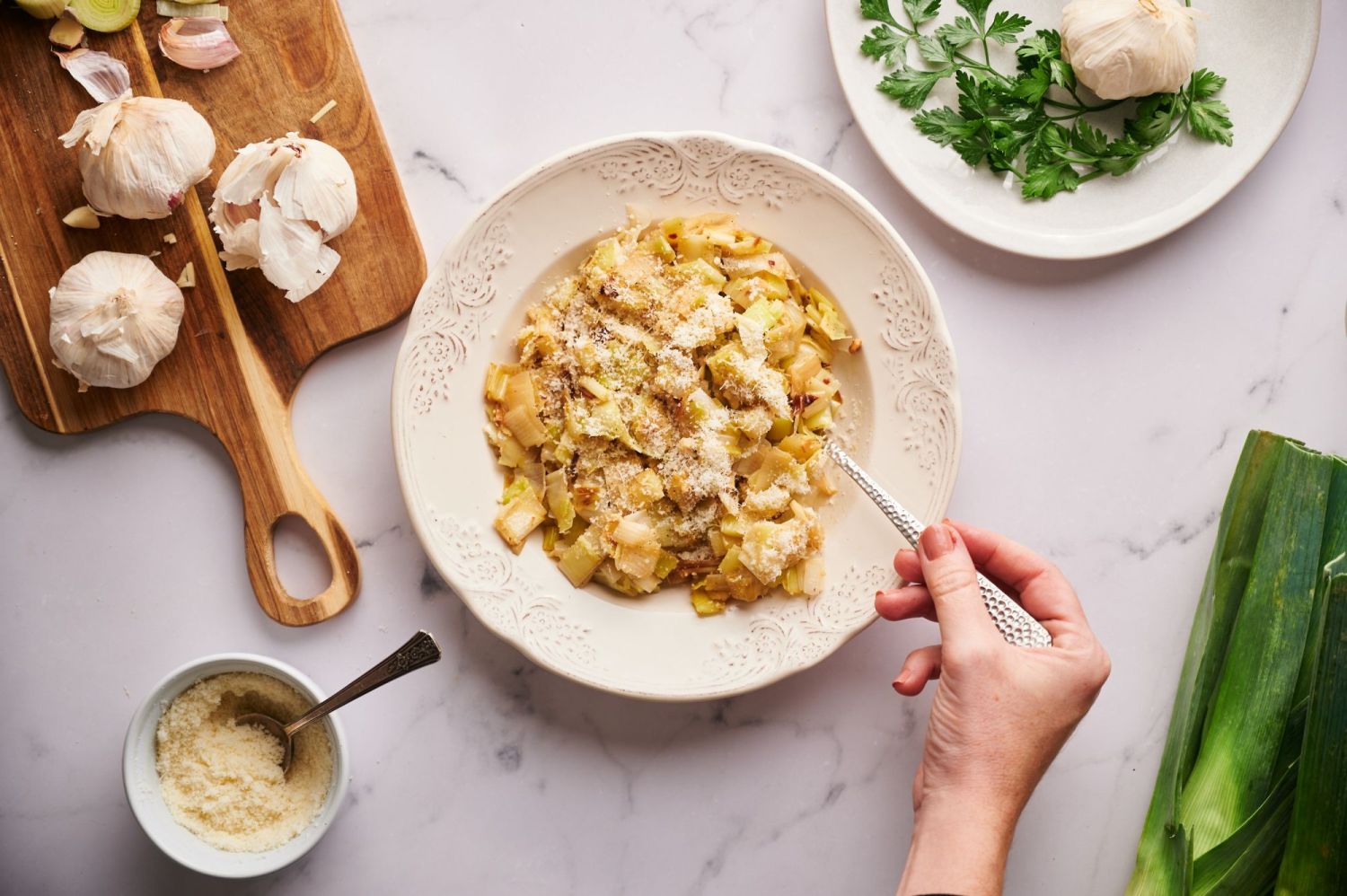 Butter sautéed leeks in a bowl topped with parmesan cheese with a silver spoon.
