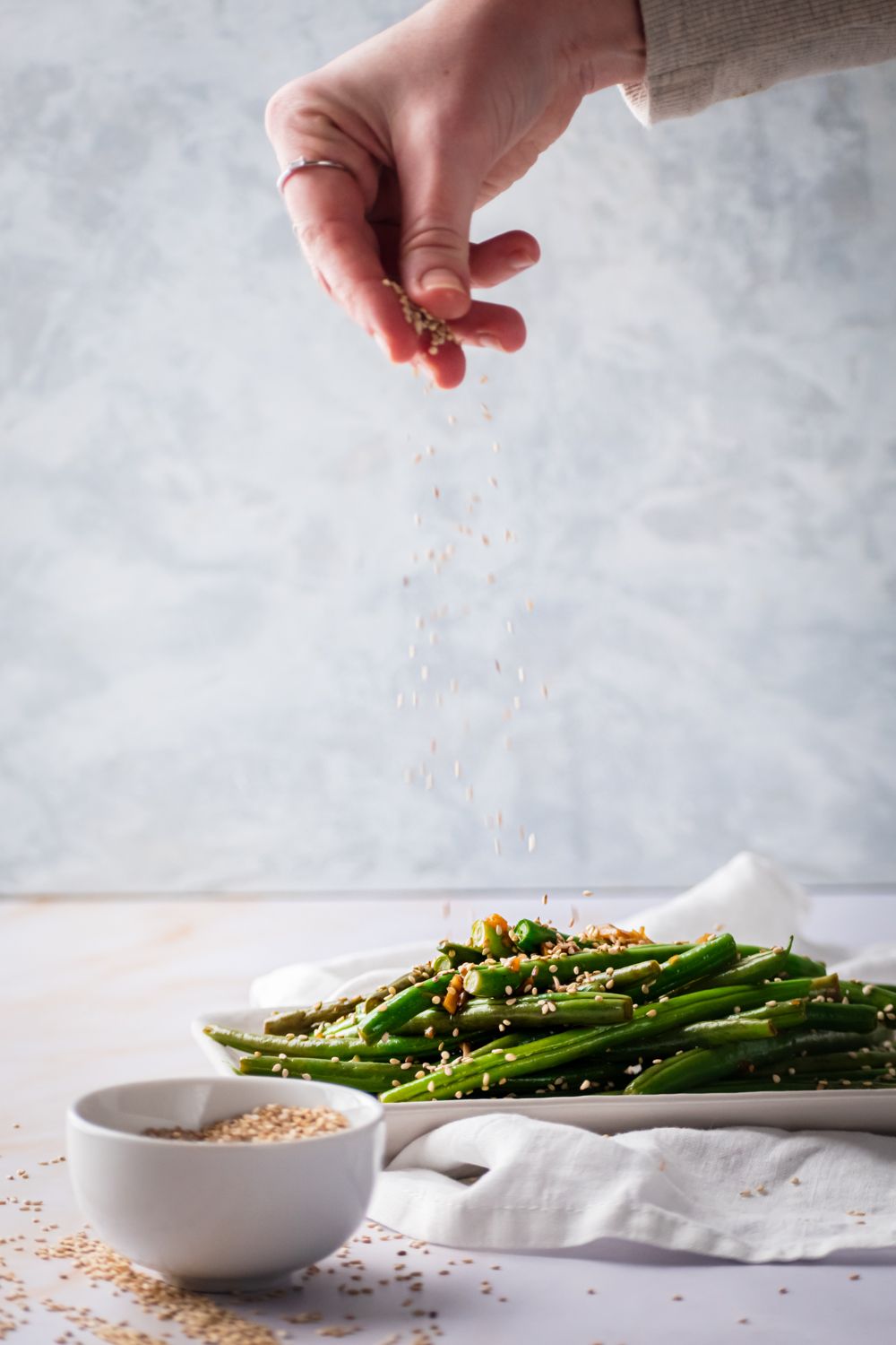 Green beans with sesame seeds being sprinkled on top.
