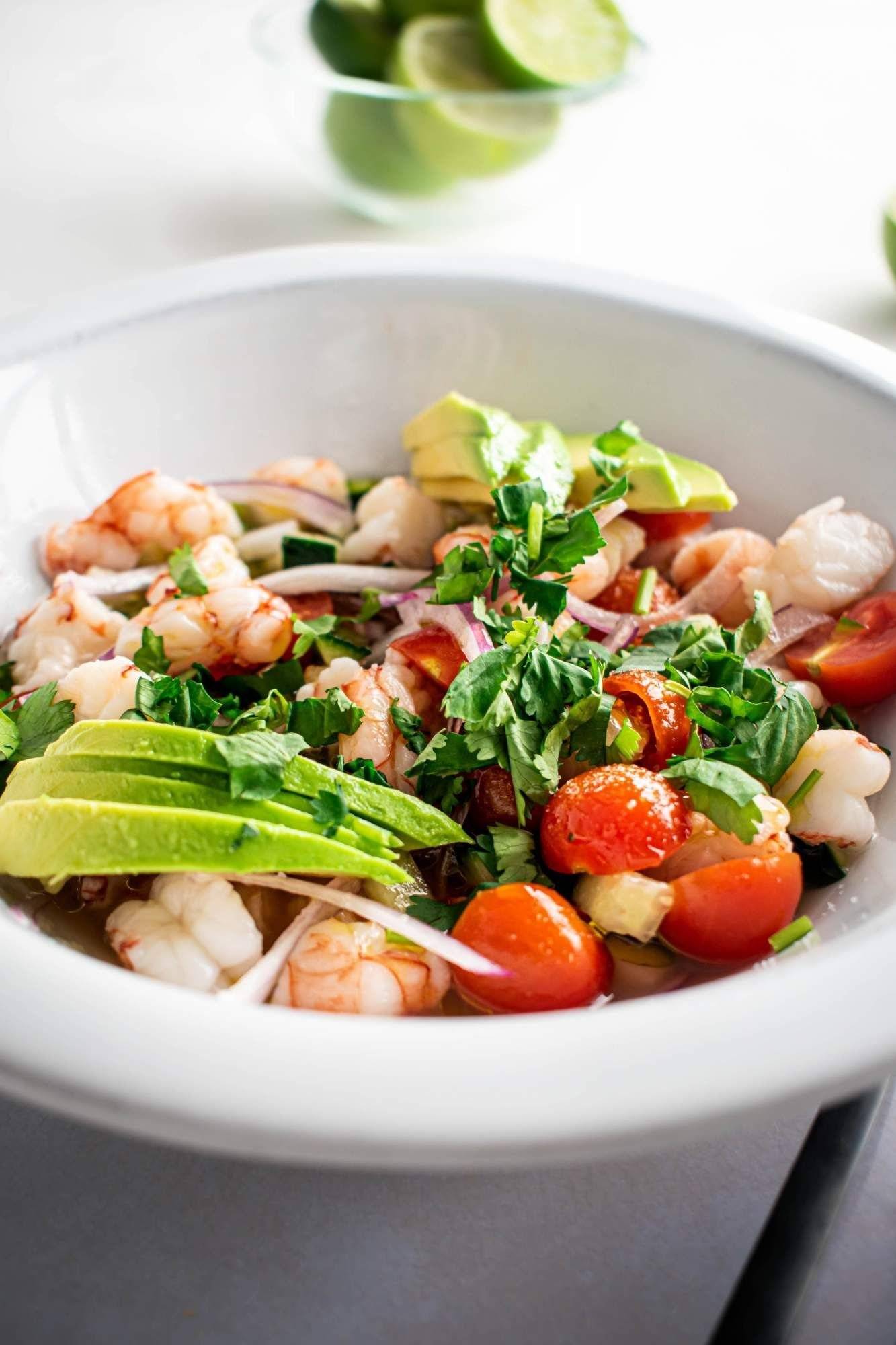 Ceviche with shrimp, avocado, tomatoes, red onion, cucumber, and cilantro in a white bowl.