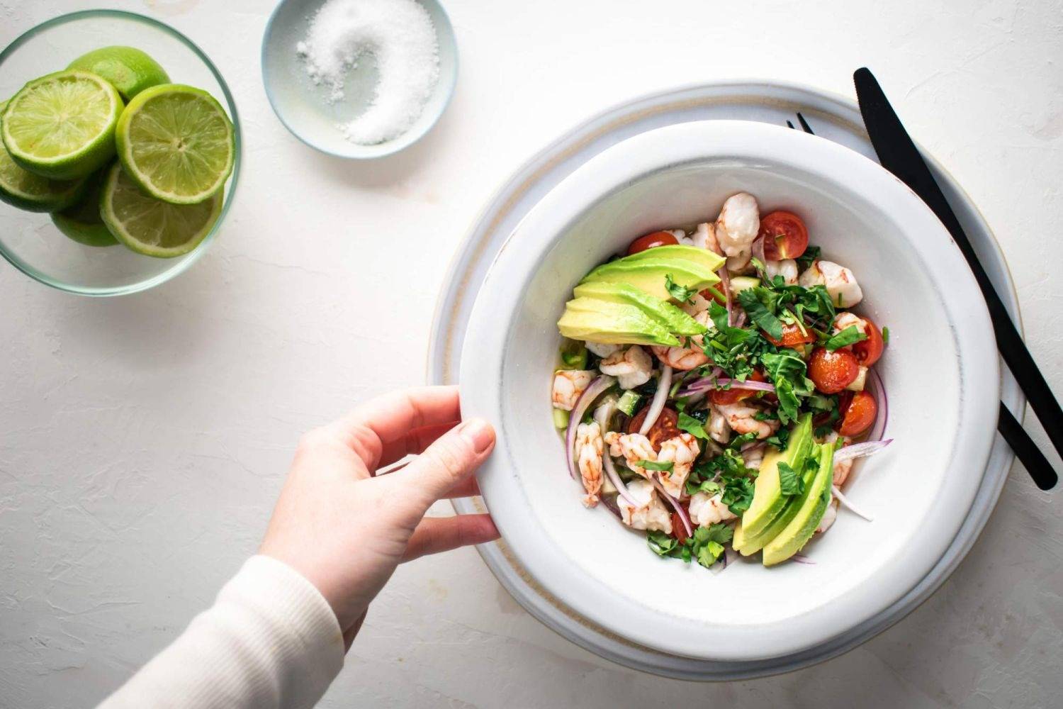 Lime shrimp ceviche topped with sliced avocado and cilantro with limes on the side.