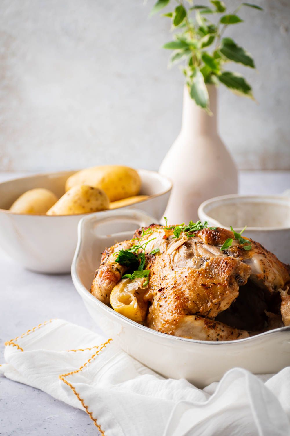Crockpot rotisserie chicken served in a white dish with slow cooker potatoes on the side.
