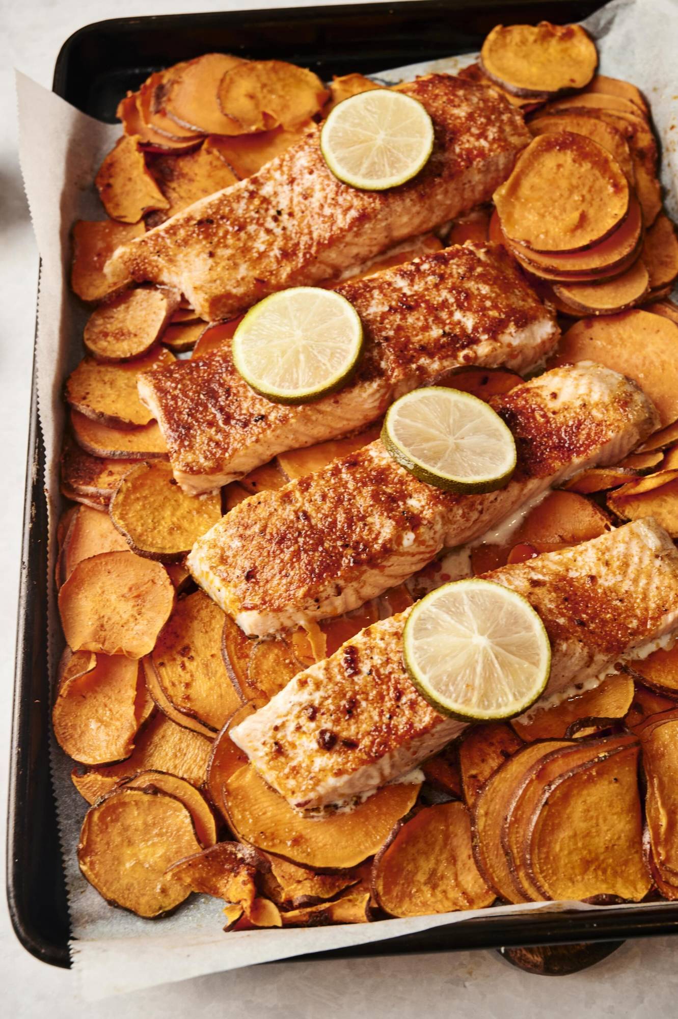 Baked salmon fillets with lime slices on a bed of roasted sweet potatoes.
