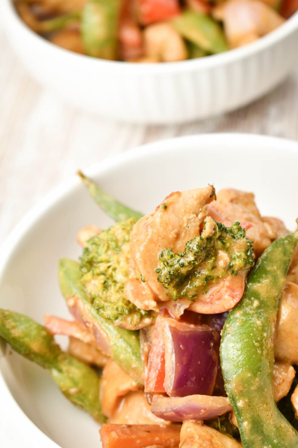 Chicken and vegetables in a spicy peanut sauce with white rice in a bowl.