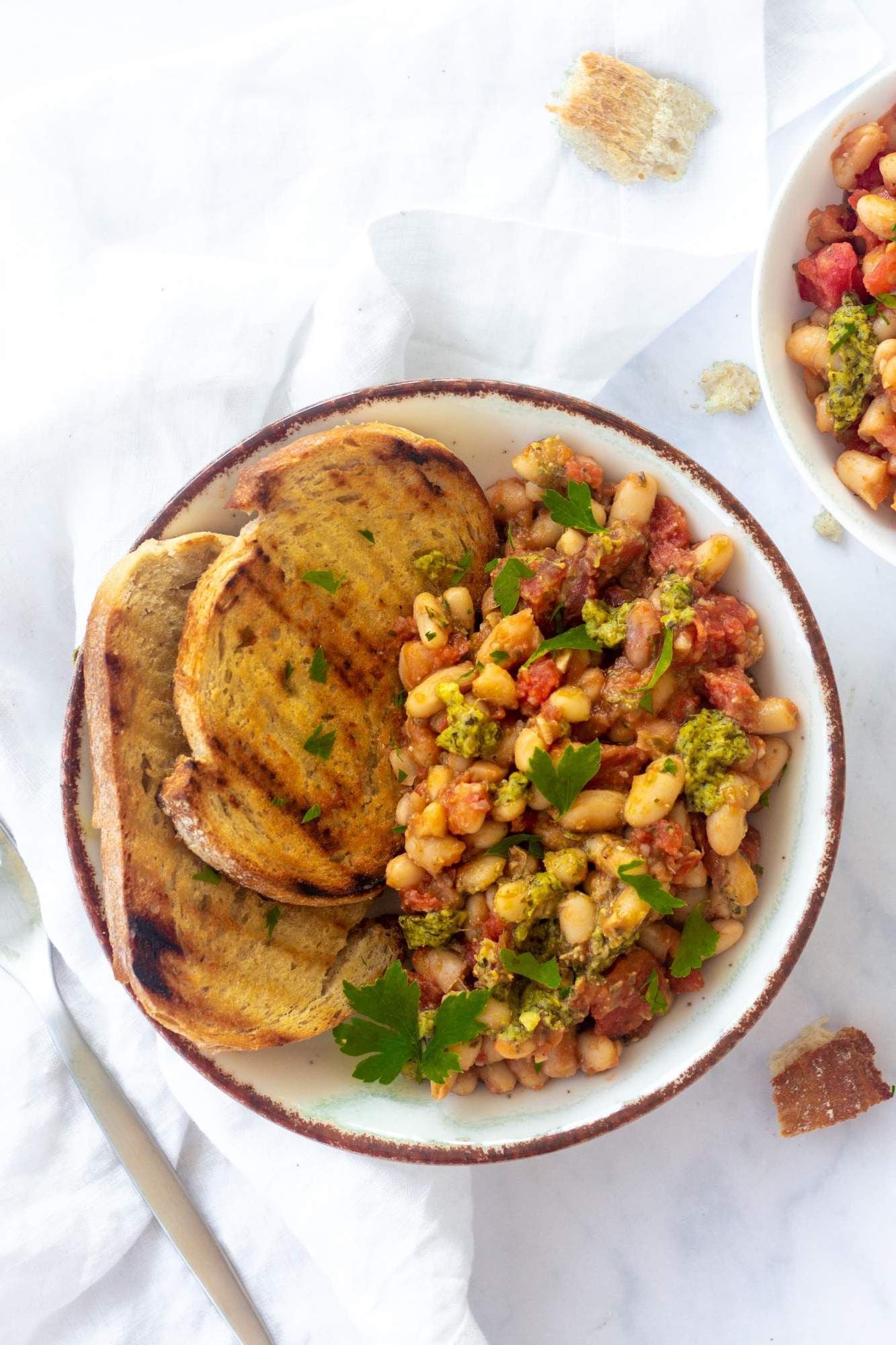 Stewed white beans with tomatoes, garlic, spices, and basil pesto on top served with garlic bread.