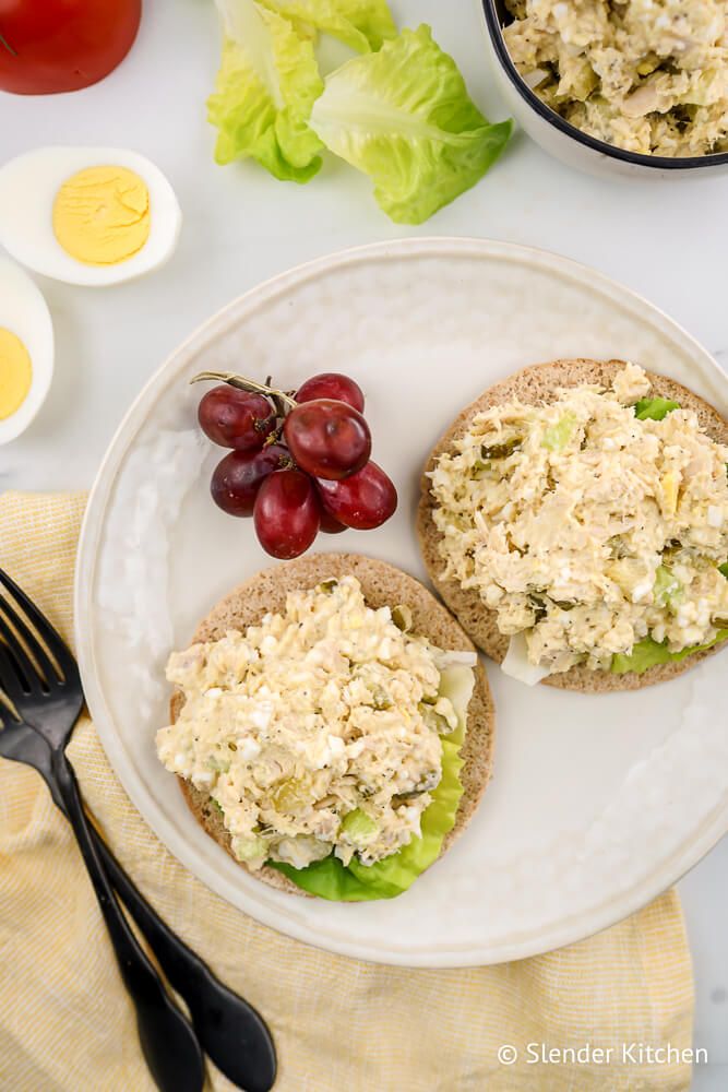 Egg and tuna salad with wheat bread, lettuce, tomatoes, and a side of grapes.