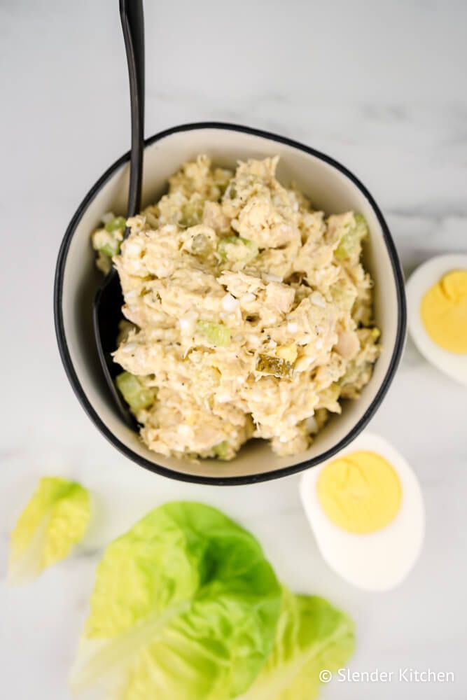 Tuna and egg salad in a bowl with dill pickles and celery.