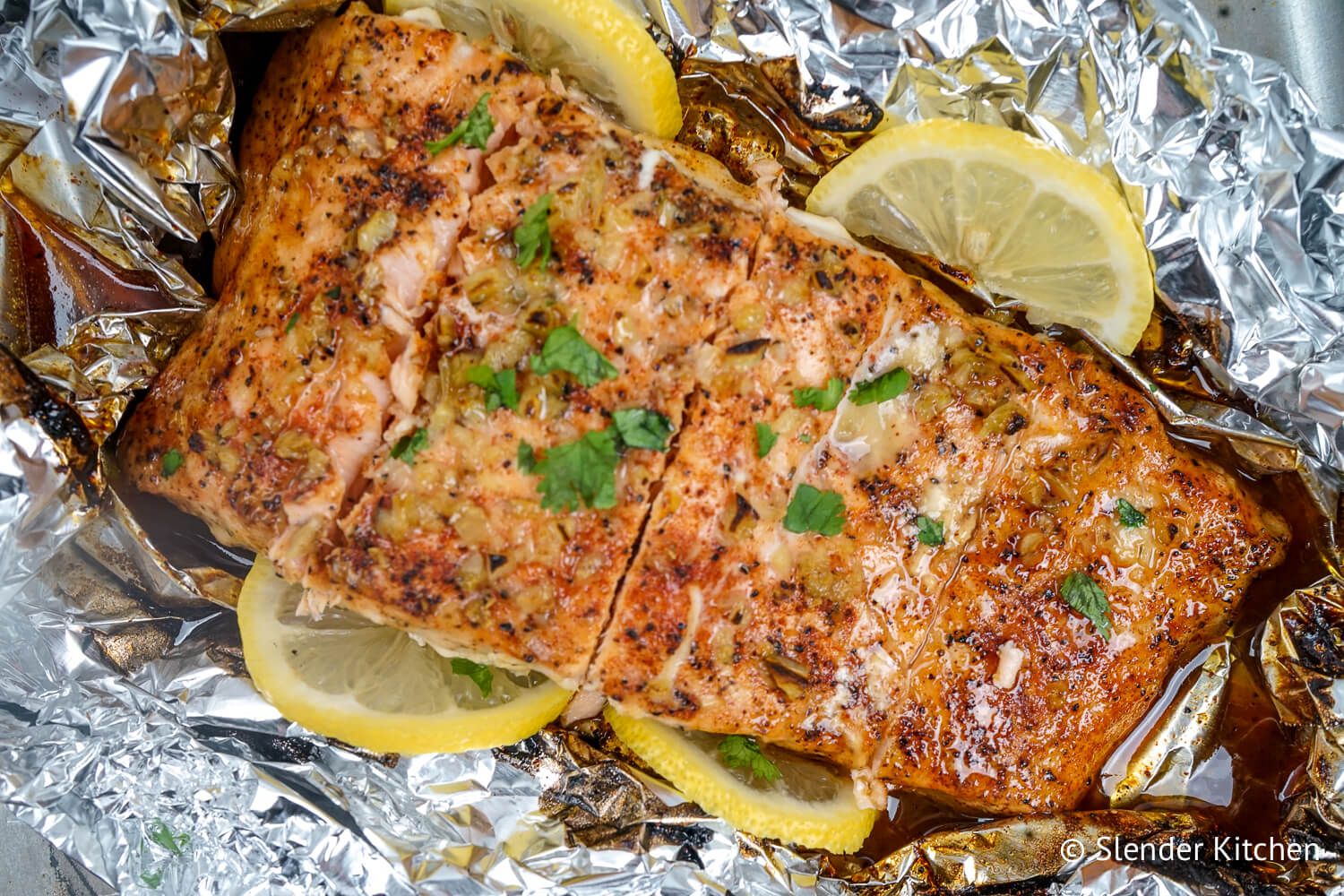 Baked garlic lemon salmon in a foil packet with fresh lemon slices and parsley.