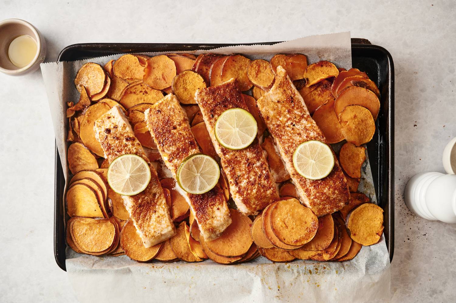 Sheet pan with baked southwest-seasoned salmon fillets on a bed of roasted sweet potato slices, garnished with lime rounds.
