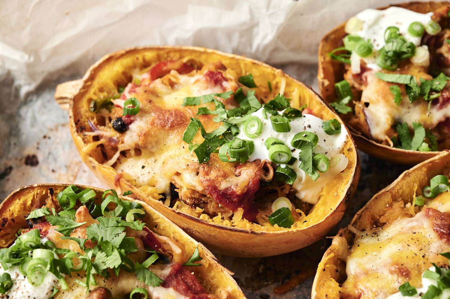 Spaghetti squash enchilada boats topped with melted cheese, sour cream, and chopped green onions.