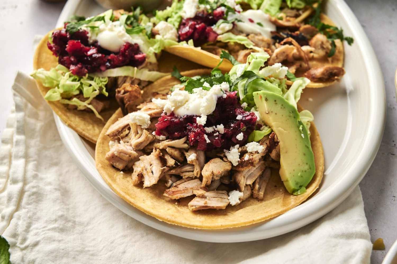 Leftover turkey tacos with cranberry relish, cilantro, avocado, and queso fresco being served on a plate.