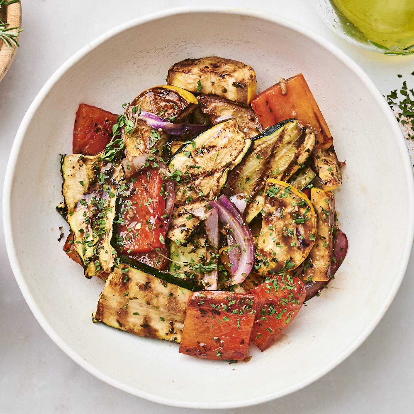 A colorful bowl of grilled vegetables, including zucchini, bell peppers, and onions, garnished with herbs and drizzled in dressing.