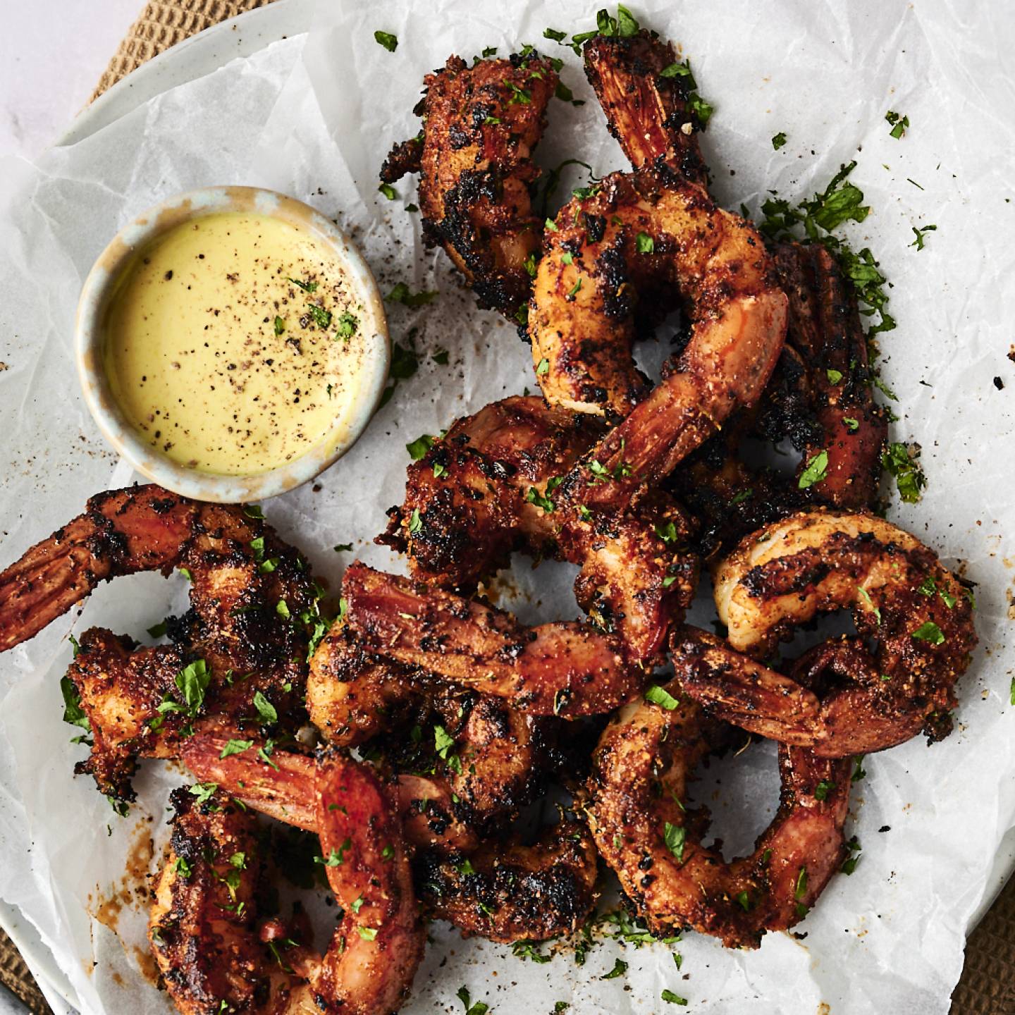 Grilled shrimp garnished with herbs, served with a creamy dipping sauce on parchment paper, ready to enjoy.