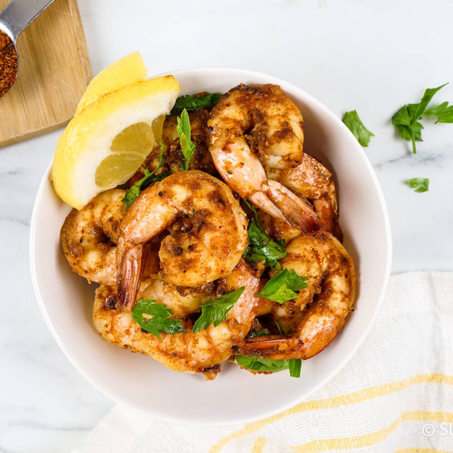 Cajun shrimp coated in seasoning in a bowl with parsley and lemon.
