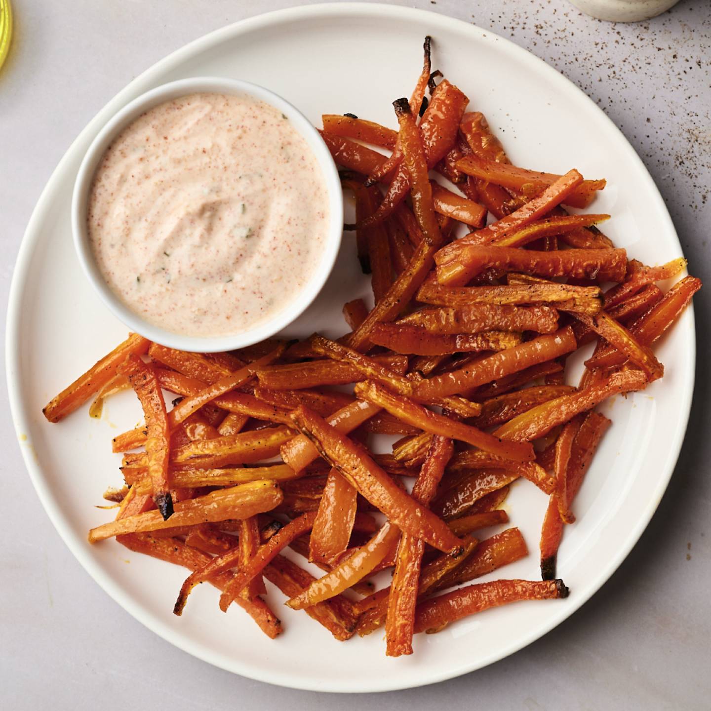 A bowl of baked carrot fries on a parchment-lined baking sheet.