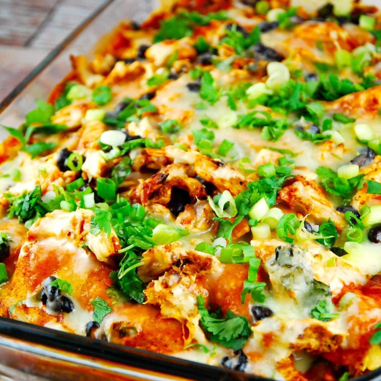 Chicken enchilada casserole with green onions and olives in a baking dish.