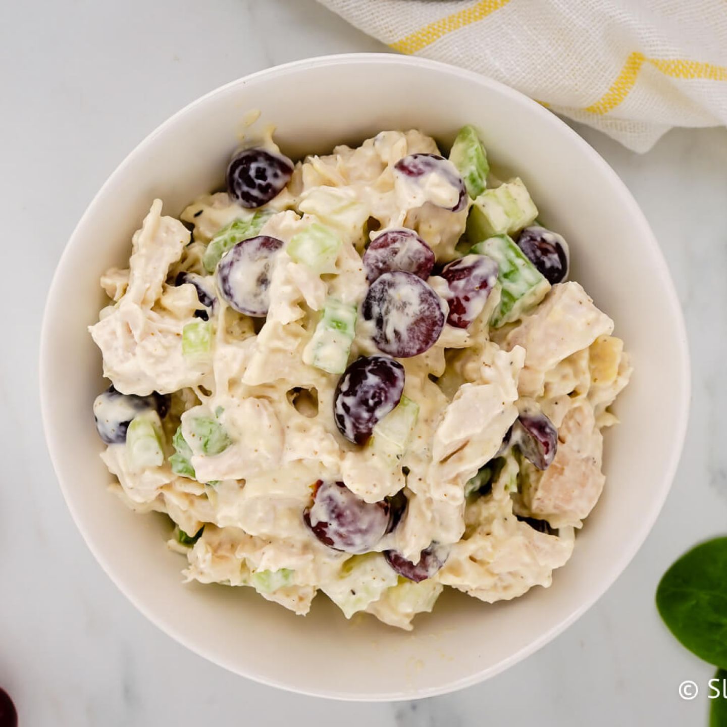Chicken salad with grapes, celery, and yogurt dressing in a bowl with grapes and spinach on the side.