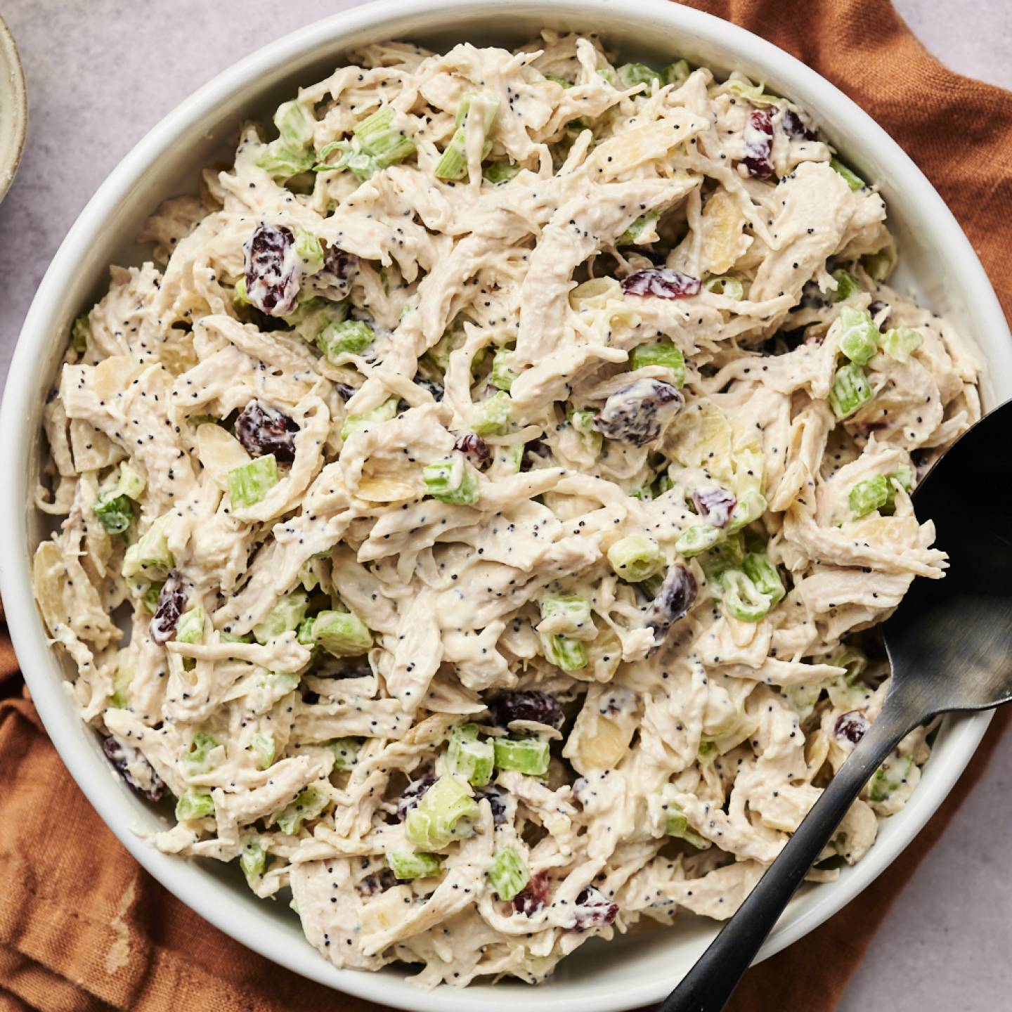 A bowl of cranberry almond chicken salad, garnished with a sprig of rosemary.