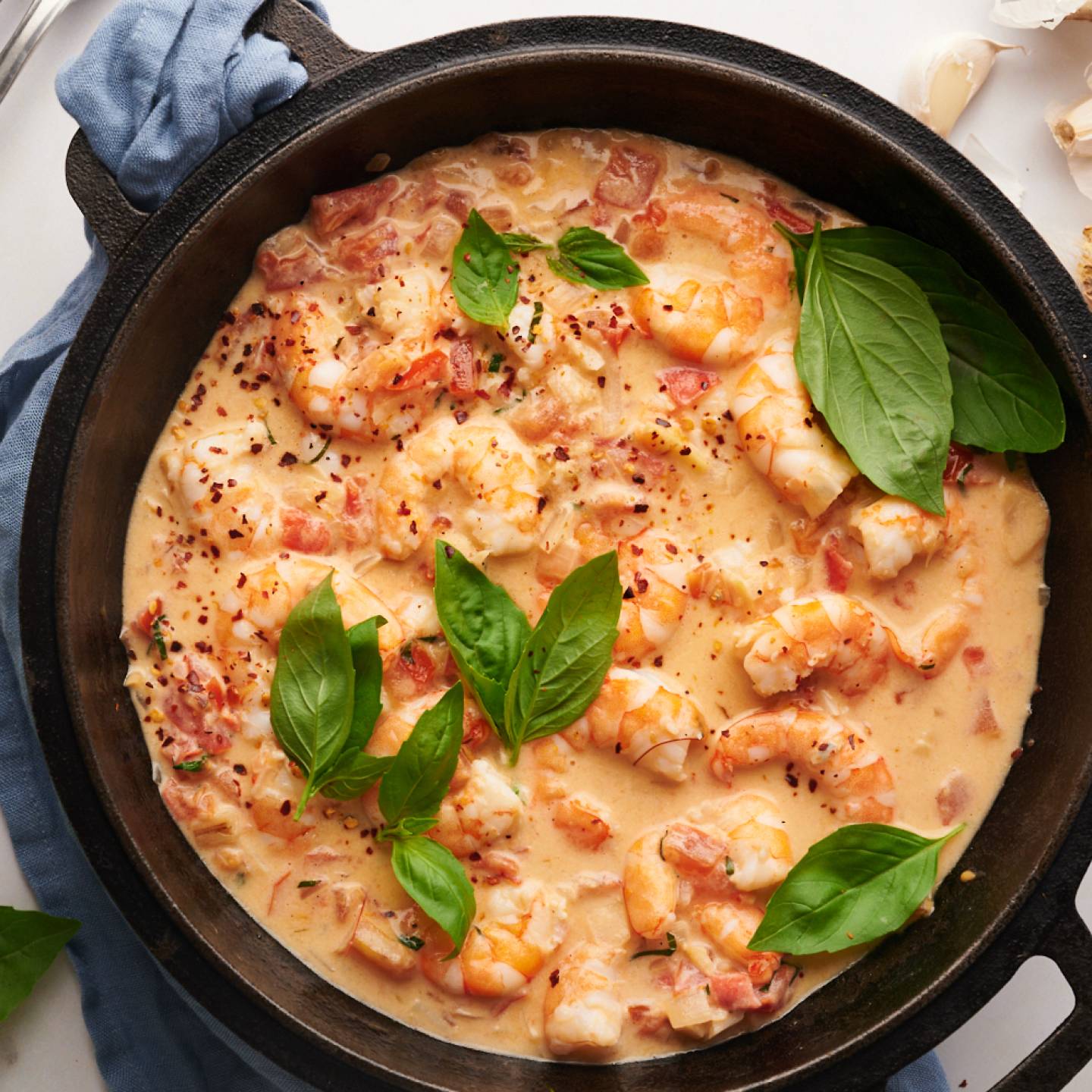 Creamy coconut shrimp with tomatoes, coconut milk, basil, and red pepper flakes in a black skillet.