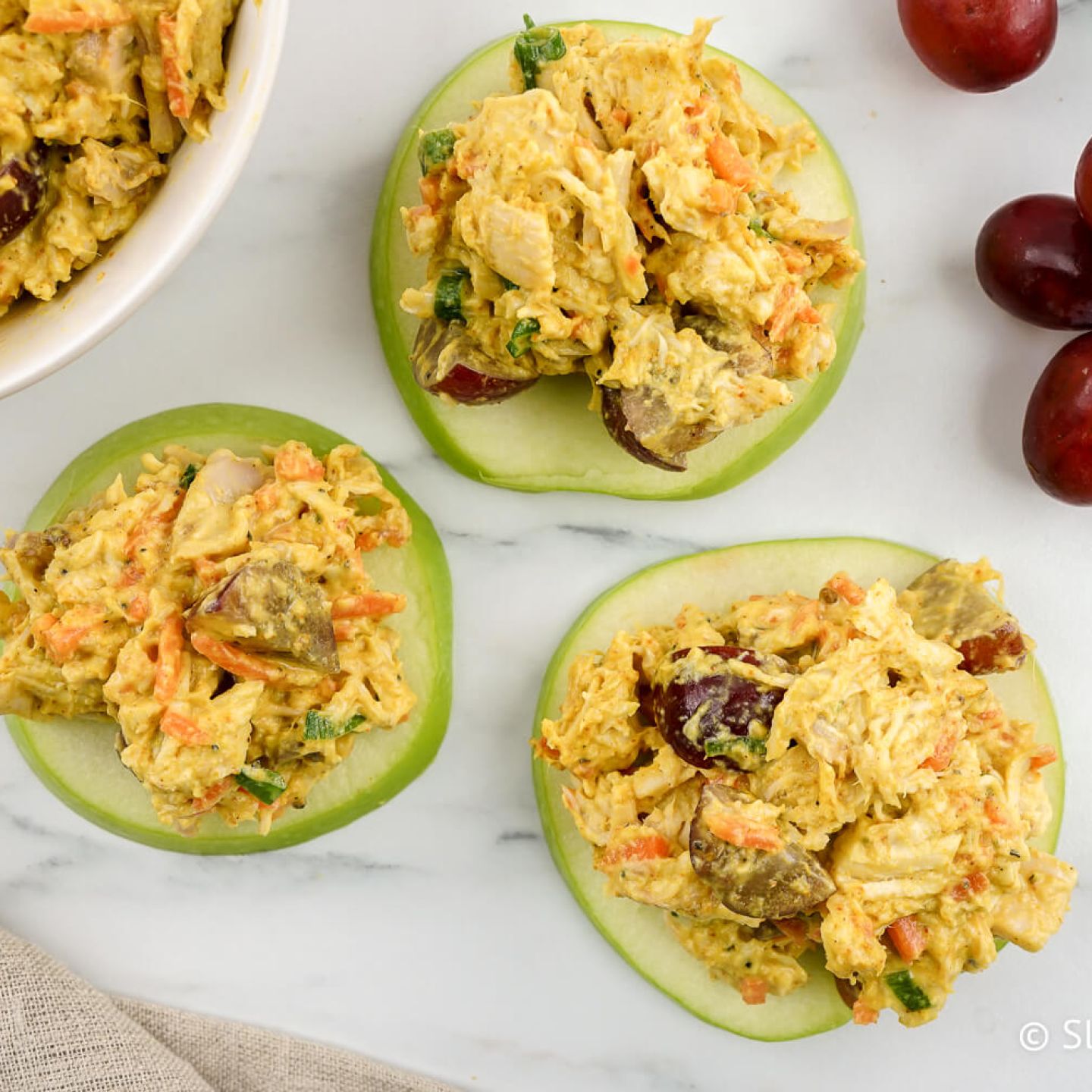 Curried chicken salad with grapes on apple slices.