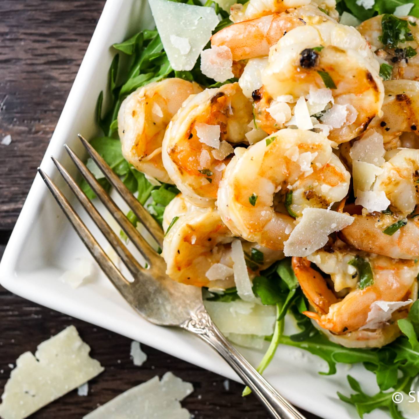 Garlic Parmesan shrimp on a plate with pieces of Parmesan cheese and greens.