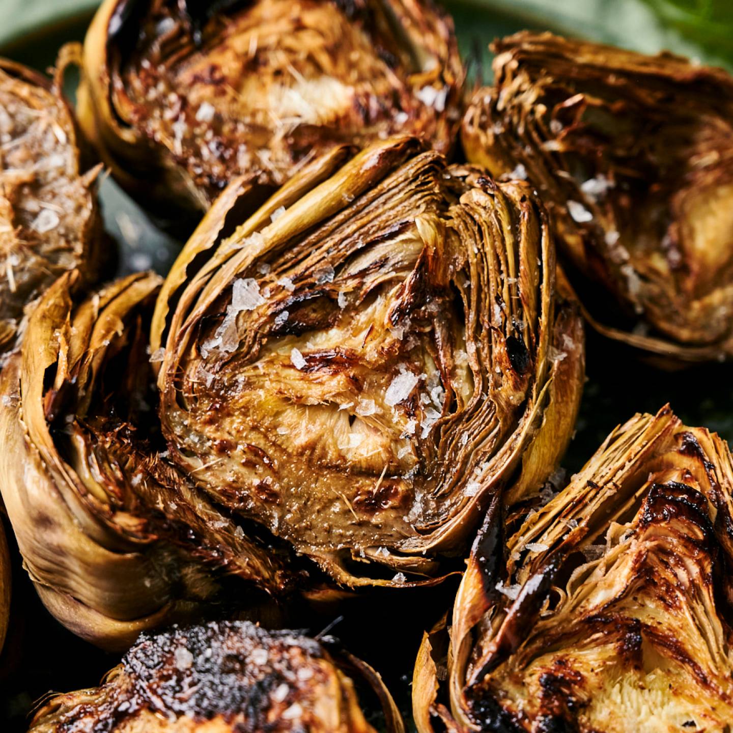 Grilled artichokes with flaky sea salt served on a plate with garlic butter.