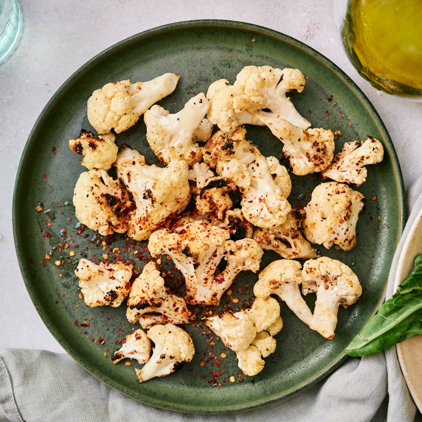 Grilled cauliflower with browned edges on a plate with red pepper flakes, salt, pepper, and olive oil.