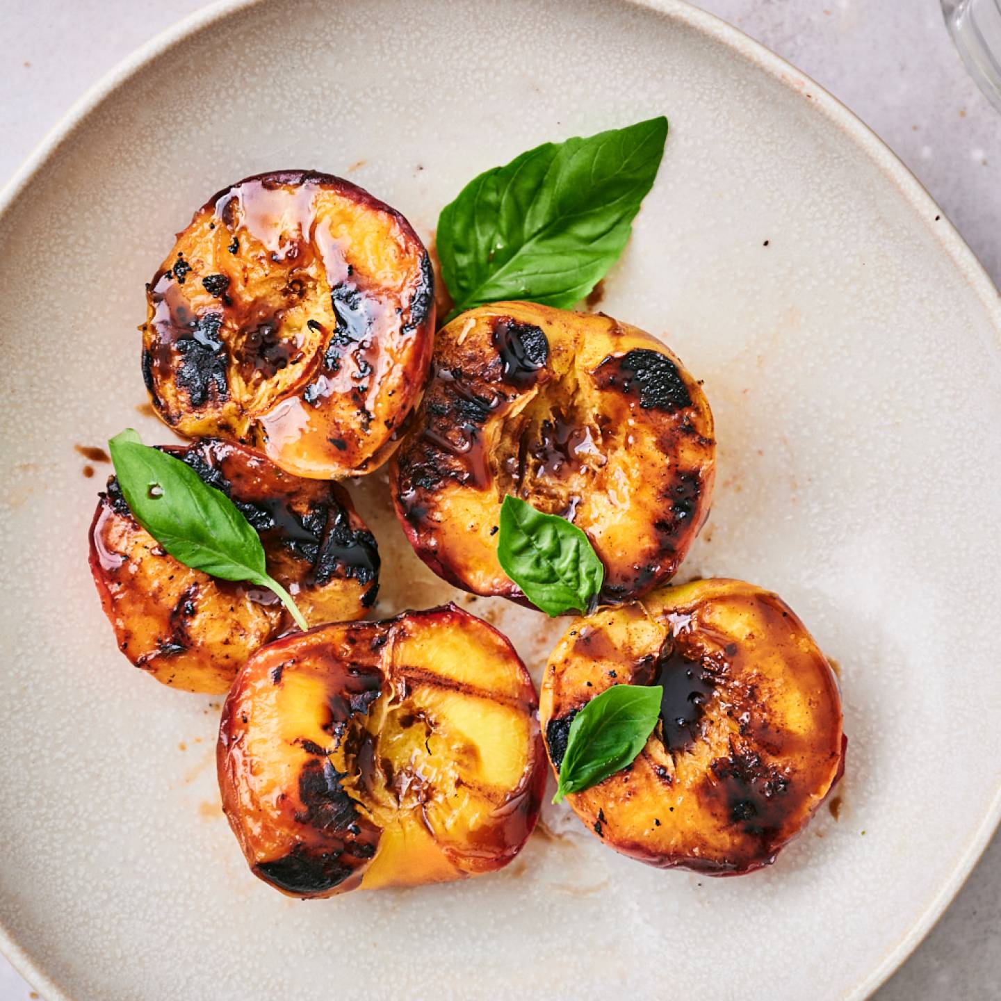Grilled peaches with dark brown grill marks served on a plate with honey and fresh basil.