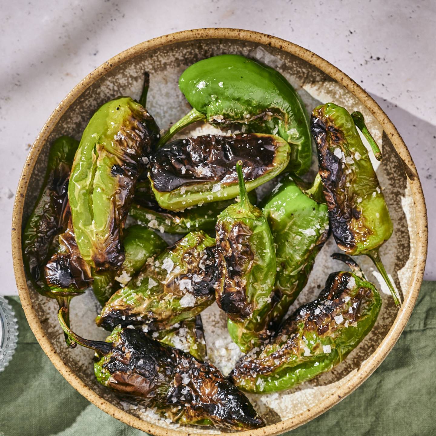 Grilled shishito peppers with blistered, charred edges served in a bowl with sea salt.