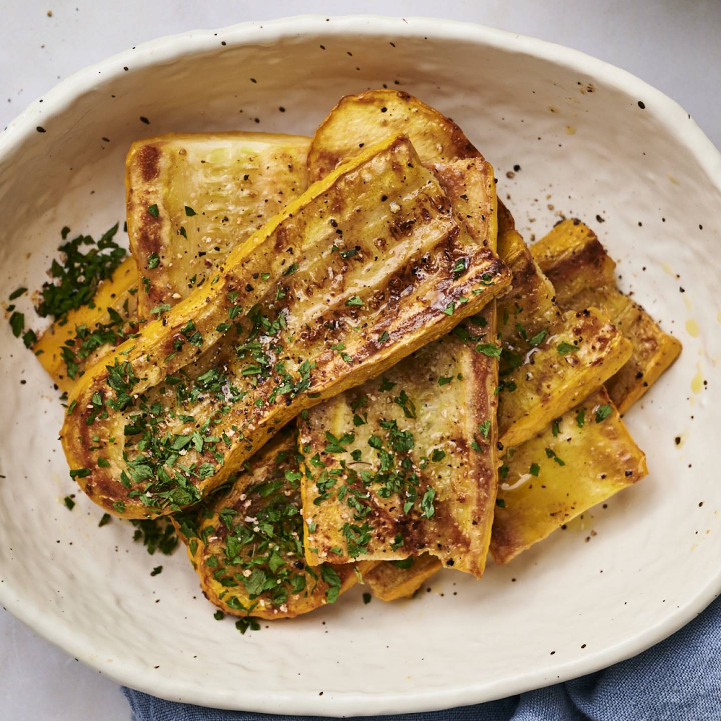 Grilled yellow squash on a black plate sprinkled with parsley.