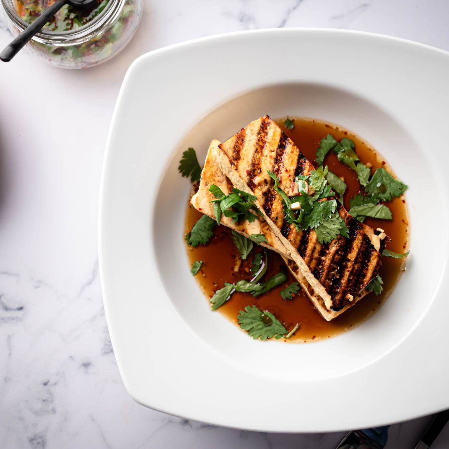 Grilled tofu in a marinade made with soy sauce served in a bowl with cilantro.