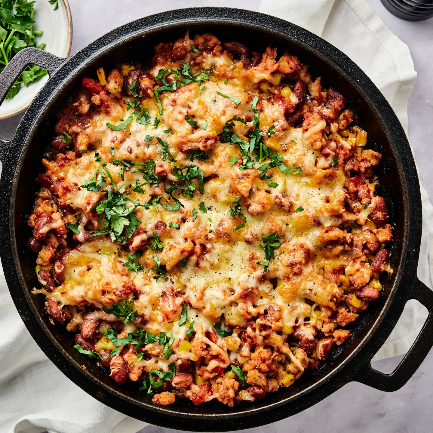 Taco casserole with pinto beans, onions, peppers, turkey, corn, salsa, and melted cheese with chips, cilantro, and jalapeno on the side.