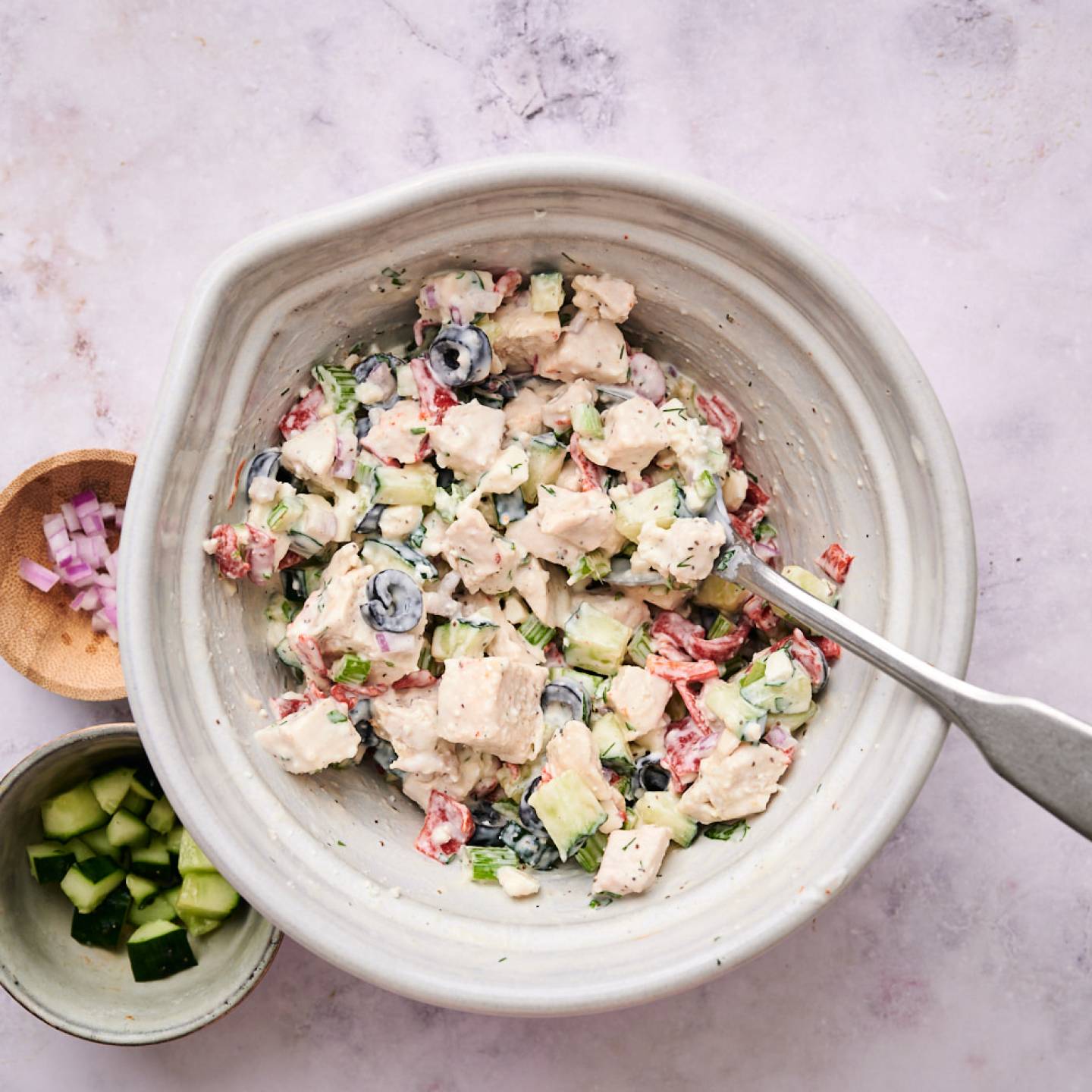 Mediterranean chicken salad with cucumbers, roasted red peppers, dill, parsley, and red onion in a bowl with lettuce on the side.