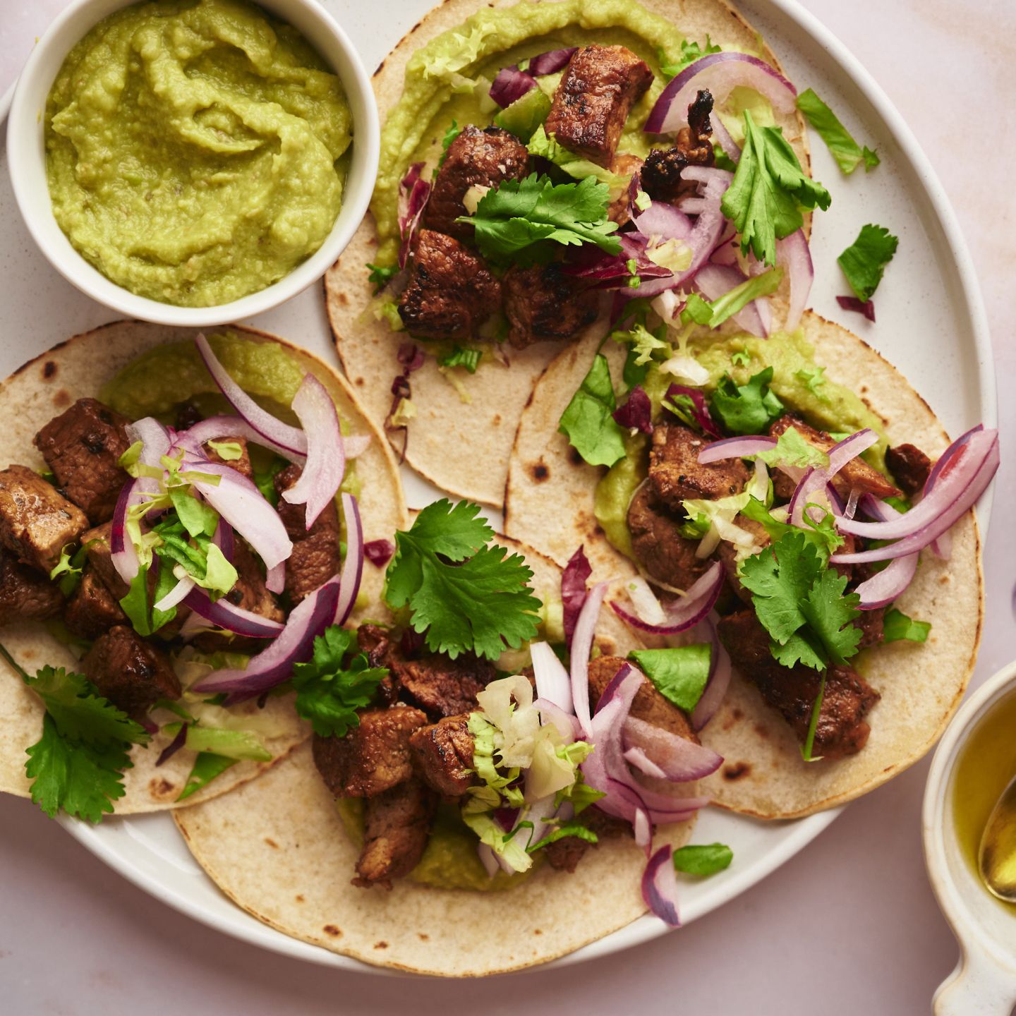 Pork tacos with crispy pork, red onions, cilantro, and avocado on a plate.
