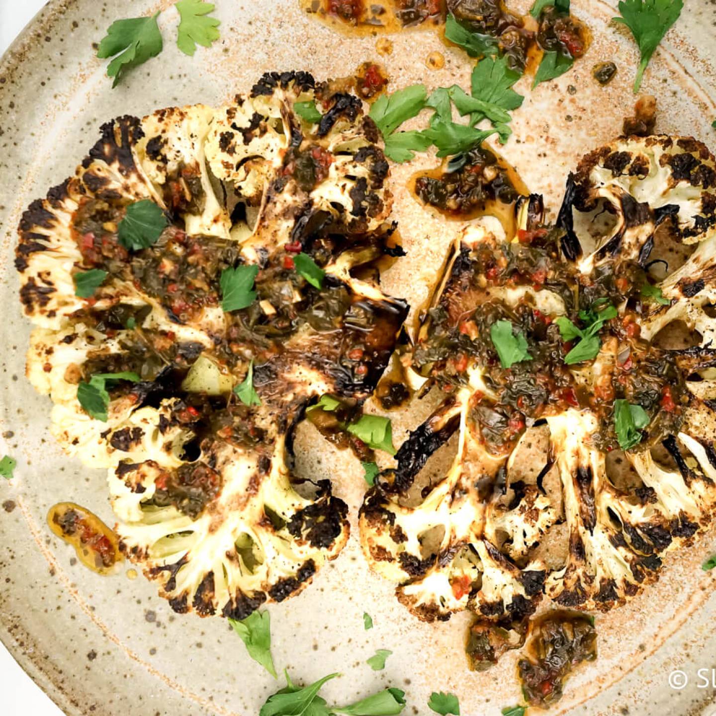 Roasted cauliflower steaks with chimichurri sauce drizzled on top.