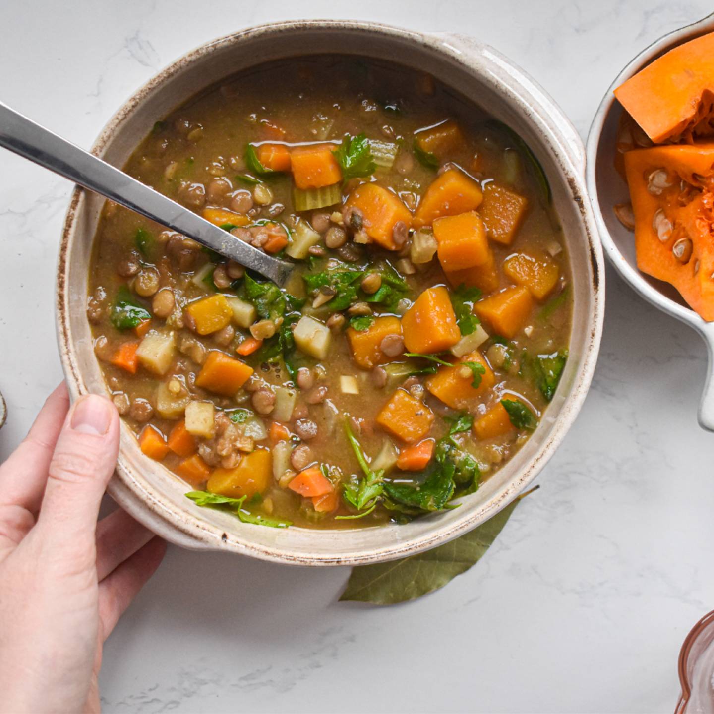 Slow cooker lentil soup with lentils, squash, carrots, spinach, and potatoes in a bowl with a hand holding it.