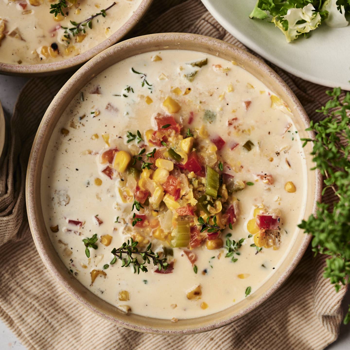 A bowl of creamy slow cooker roasted corn chowder topped with roasted vegetables, fresh thyme, and black pepper.
