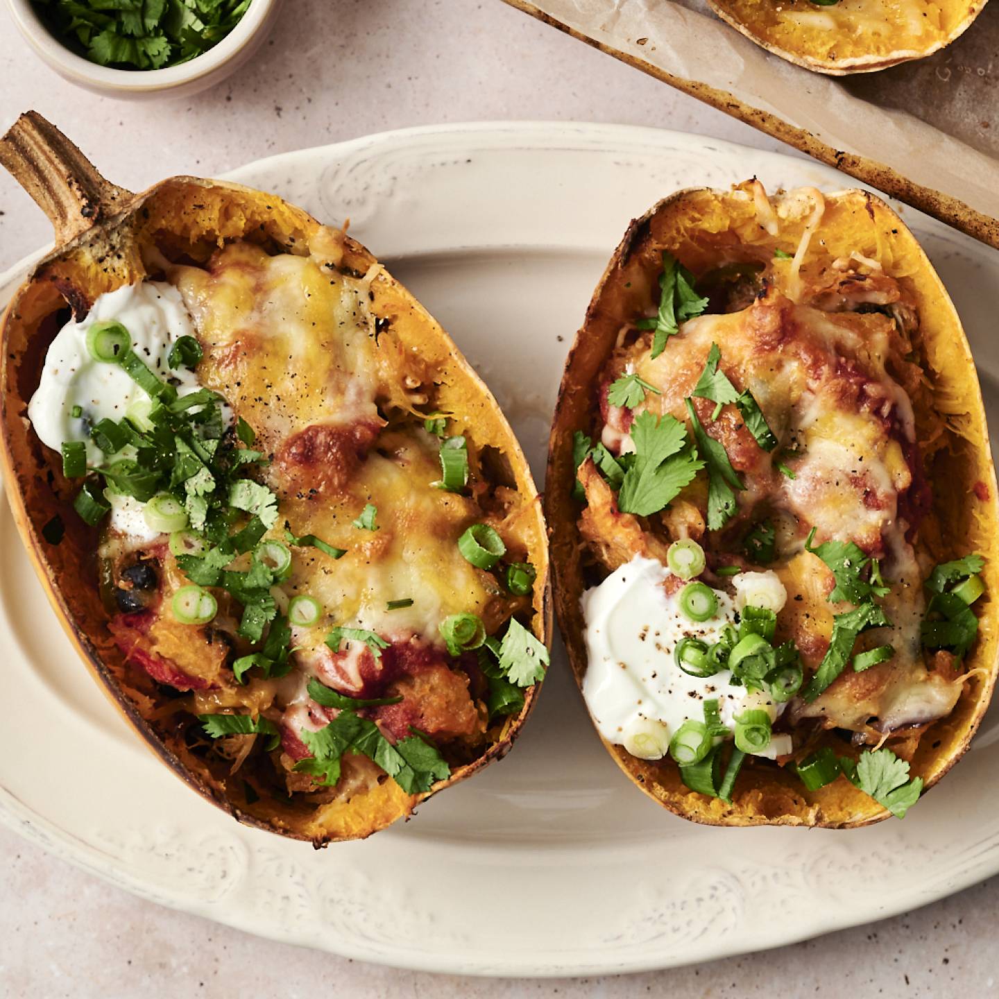 Two spaghetti squash enchilada boats topped with melted cheese, sour cream, green onions, and cilantro on a white plate.