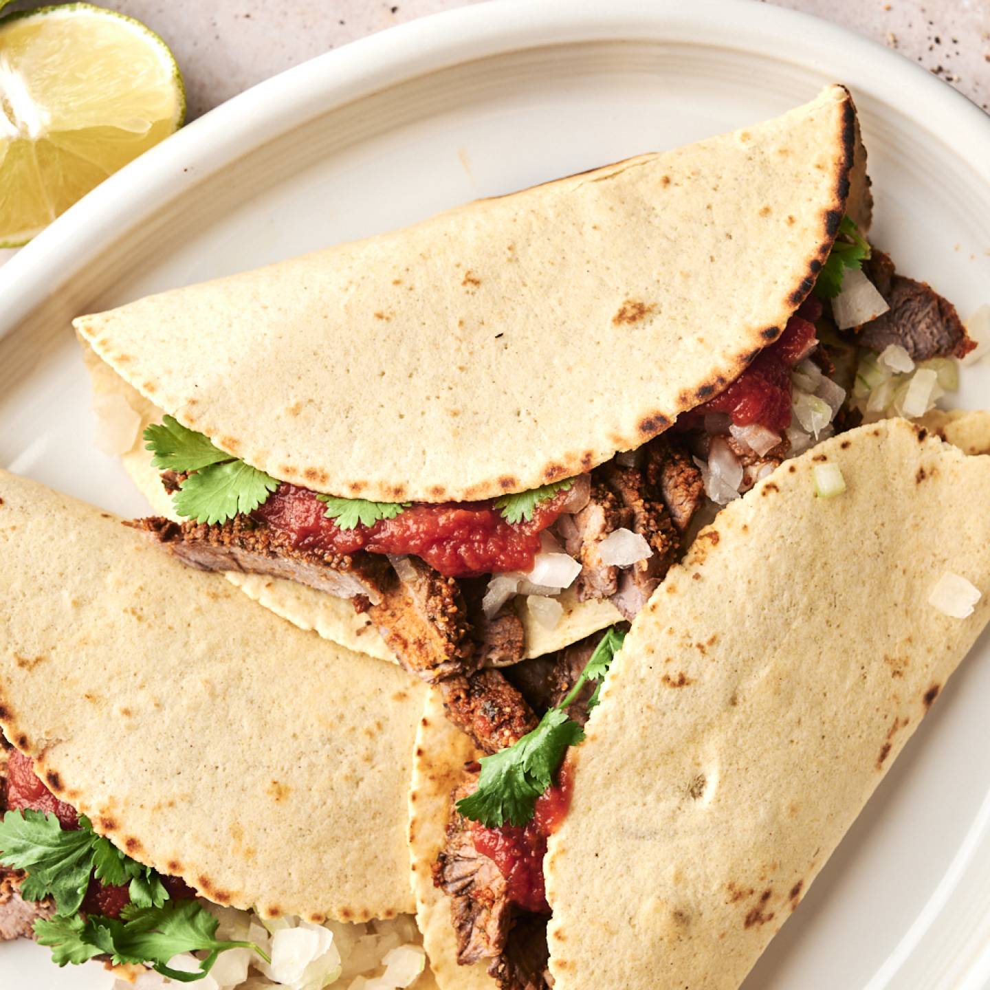 Overhead view of assembled steak tacos filled with grilled beef, onions, salsa, and fresh cilantro on a white oval platter.