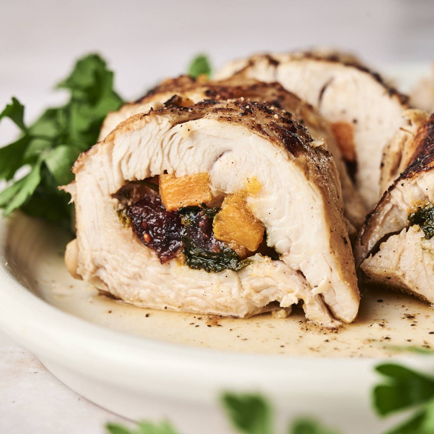 Stuffed turkey tenderloin with sweet potatoes, spinach, and dried cranberries sliced and served on a plate with parsley. 