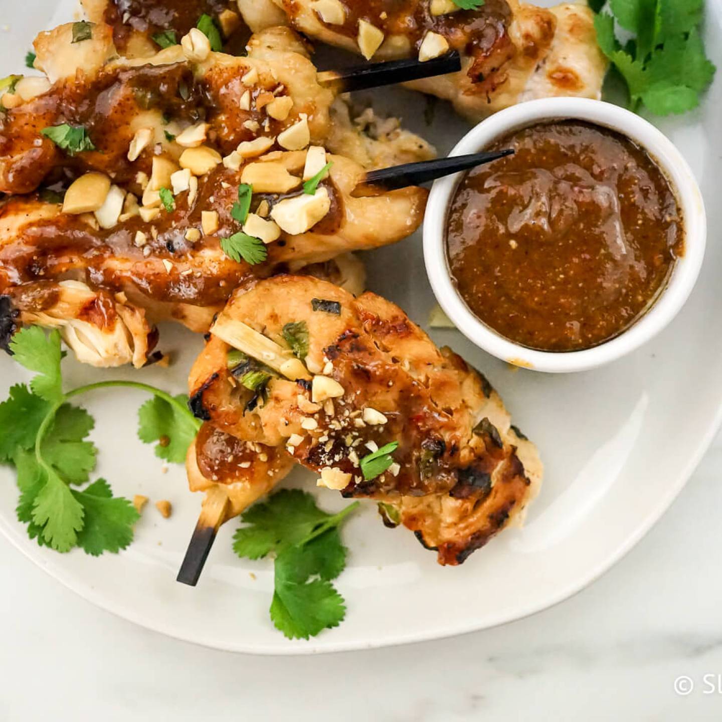 Thai peanut chicken skewers with green onions and peanut sauce on a plate.