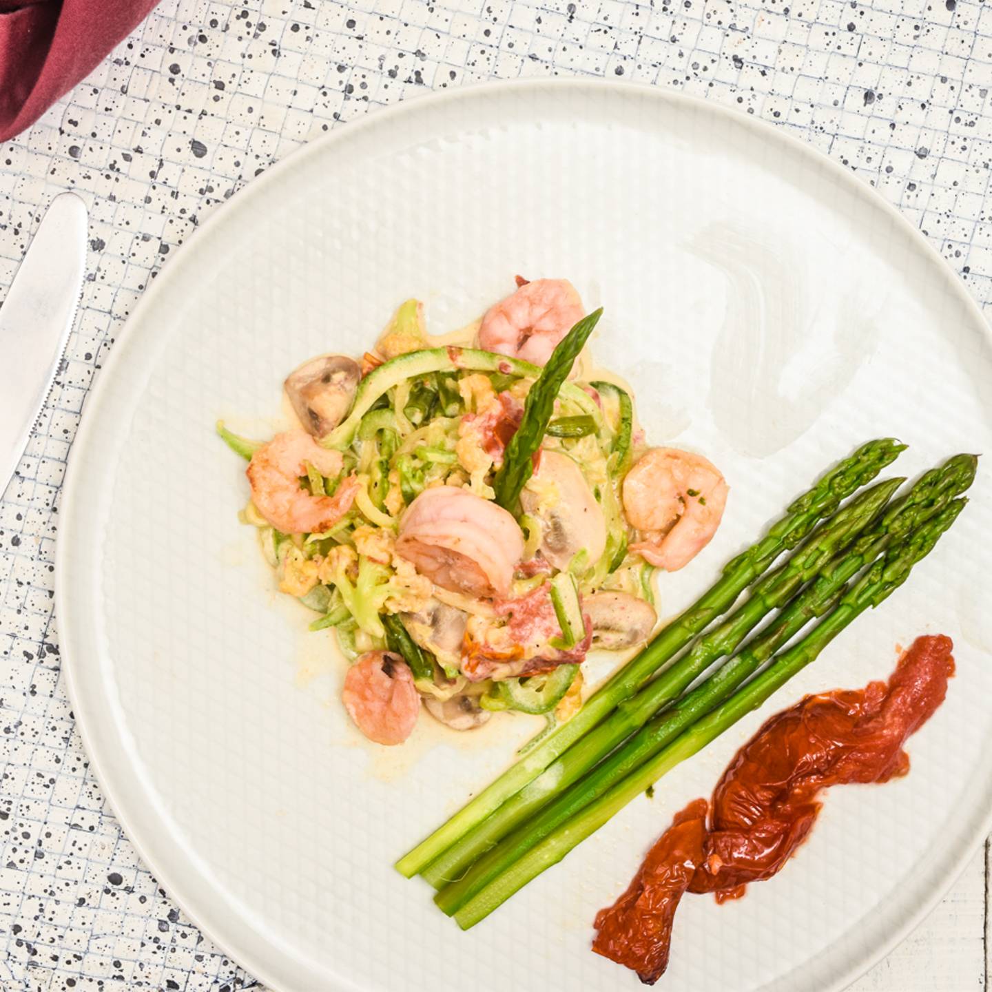 Zucchini noodle alfredo with shrimp, mushrooms, tomatoes, cauliflower, sun dried tomatoes, and more on a plate.