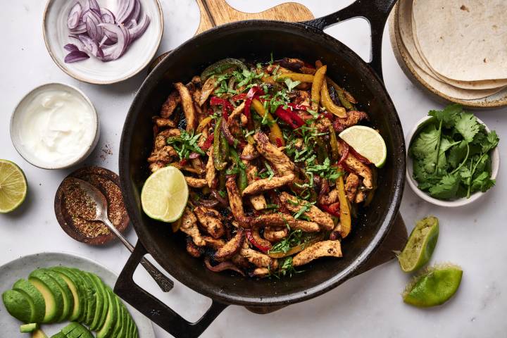 Chicken fajitas in a cast iron skillet with charred chicken, bell peppers, onions, cilantro, and lime juice.