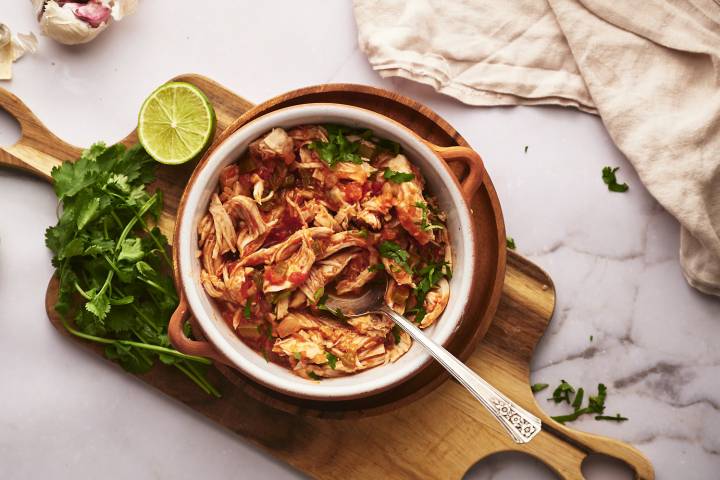 Chicken tinga in a bowl with onions, cilantro, avocado, and queso fresco.