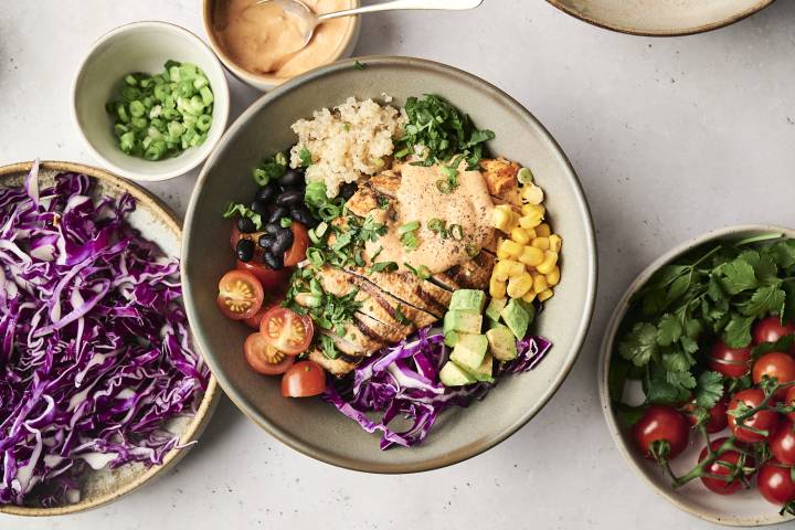 A chicken chipotle ranch bowl topped with creamy ranch sauce, sliced tomatoes, black beans, corn, avocado, red cabbage, and green onions.