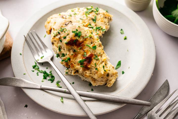 Creamy baked Parmesan chicken breasts in a casserole dish, garnished with chopped parsley.