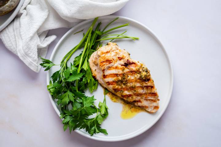 Grilled chicken breast with herb seasoning, served on a white plate with fresh parsley. Simple and appetizing presentation on a light background.