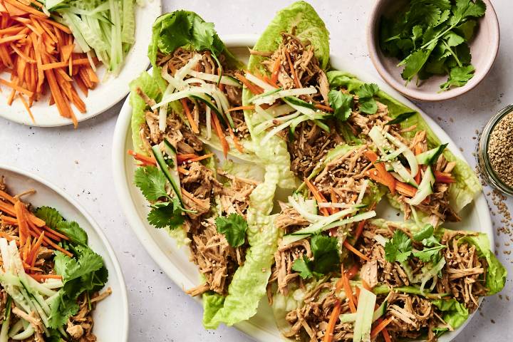 A platter of lettuce wraps filled with shredded chicken, carrot and cucumber julienne, topped with sesame seeds and fresh cilantro.